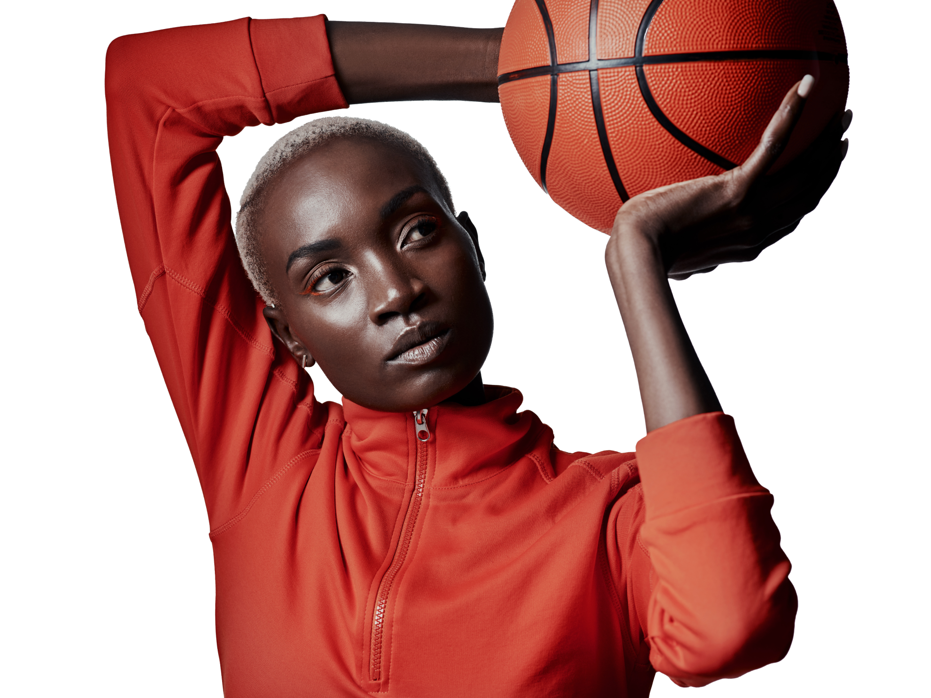 A person with a short haircut holds a basketball near their face, wearing an orange long-sleeved top and black shorts.
