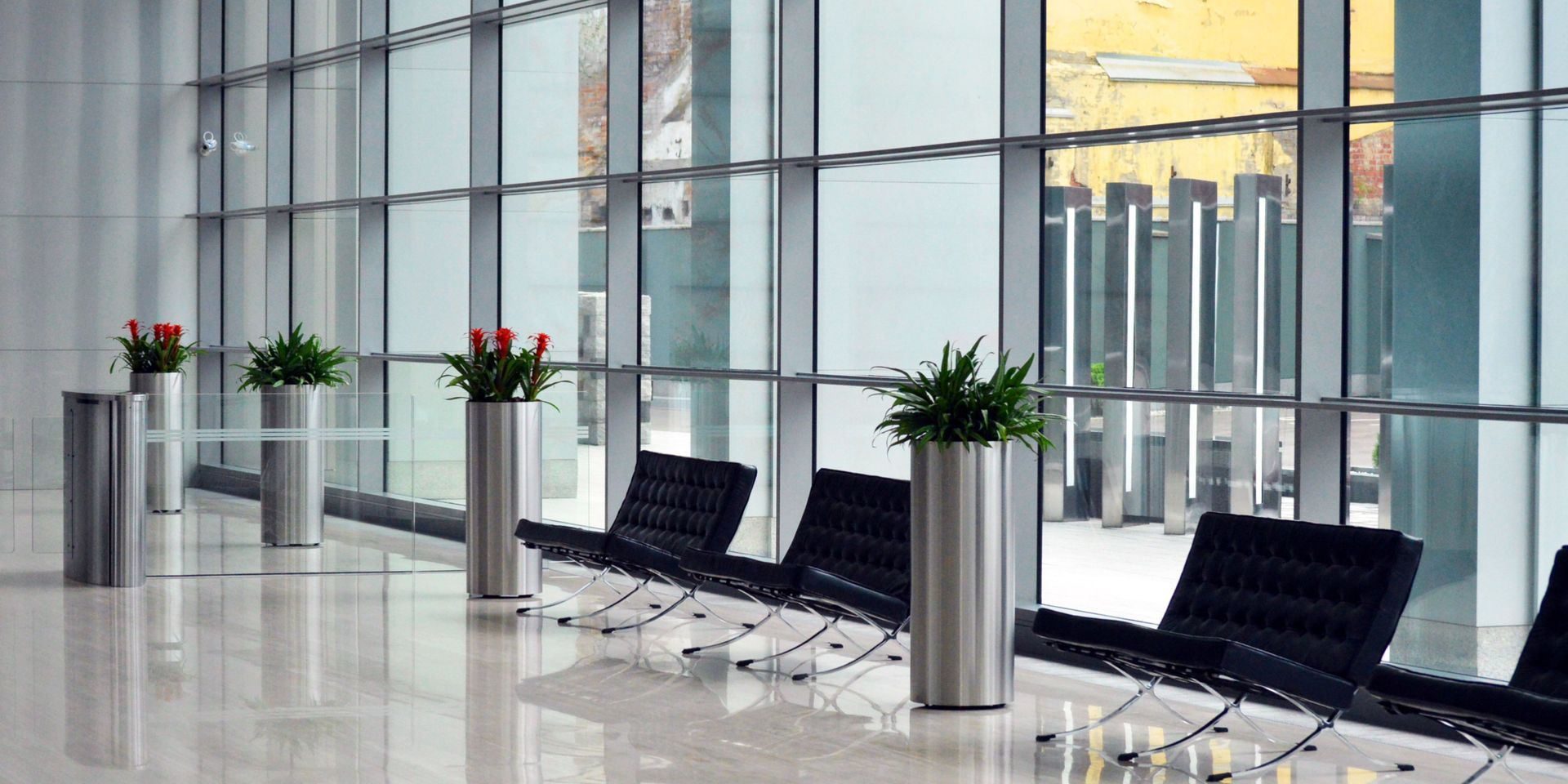 A row of chairs and planters in a lobby with lots of windows.