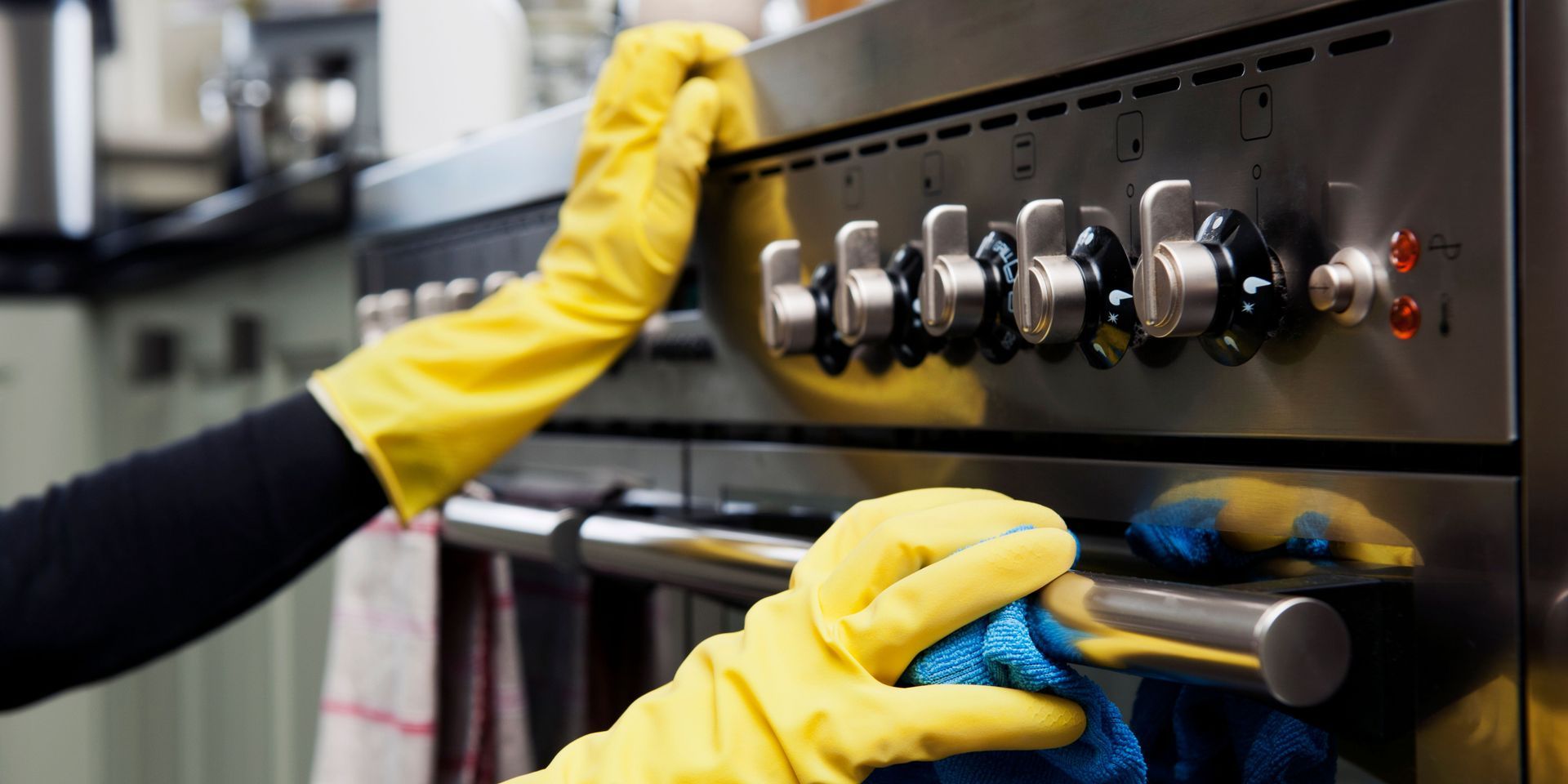 A person wearing yellow gloves is cleaning a stove with a cloth.