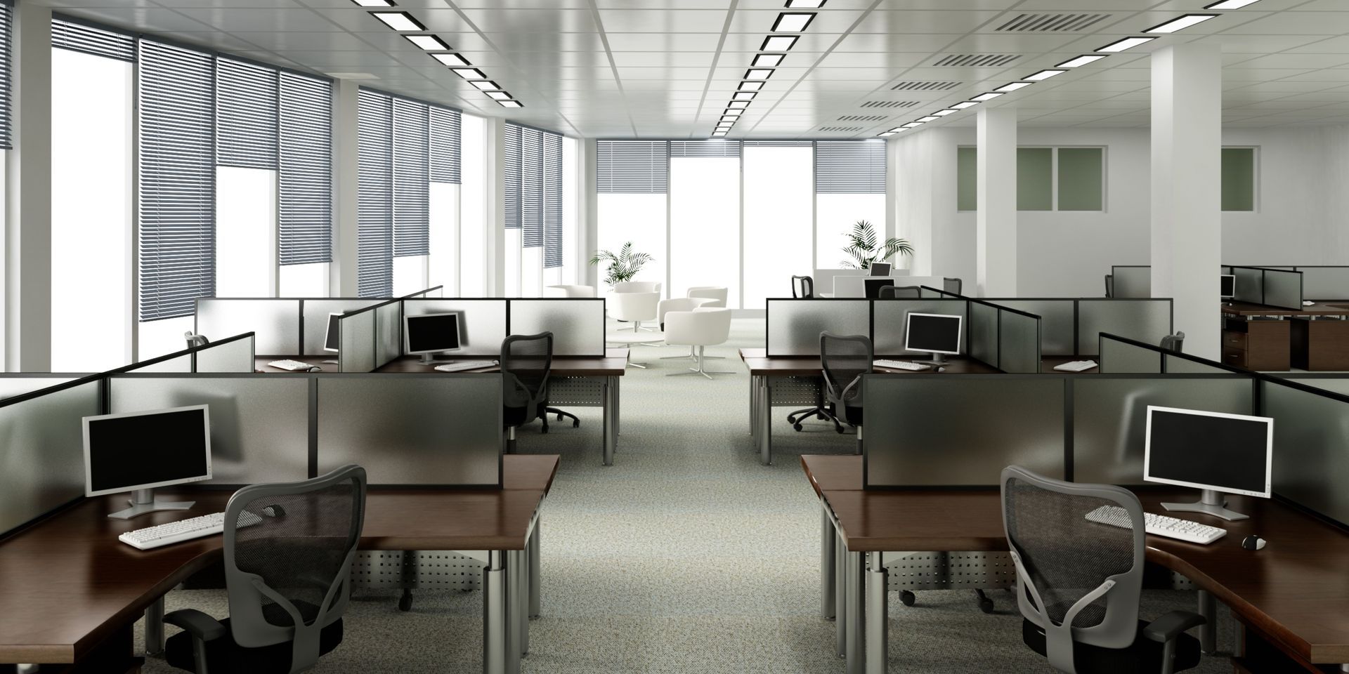 An open-plan office with cubicles, computers, and chairs. Natural light streams in through large windows.