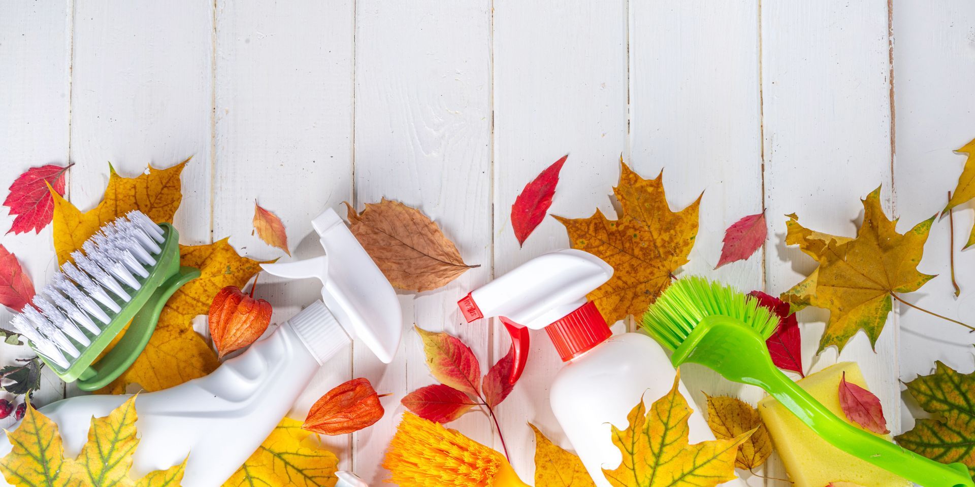 Cleaning supplies and autumn leaves on a white wooden table.