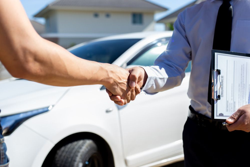 Two People Are Shaking Hands  in Front of a White Car — Duffys Car Rentals in Tablelands, QLD
