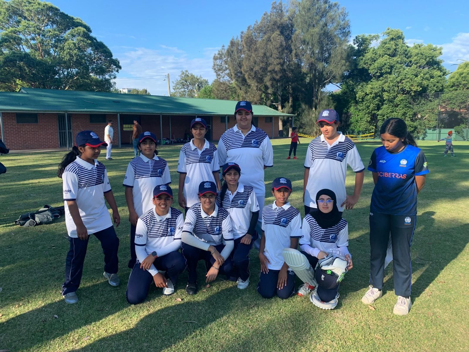 Seven female cricket players in uniform, standing on a cricket field, posing for a photo.