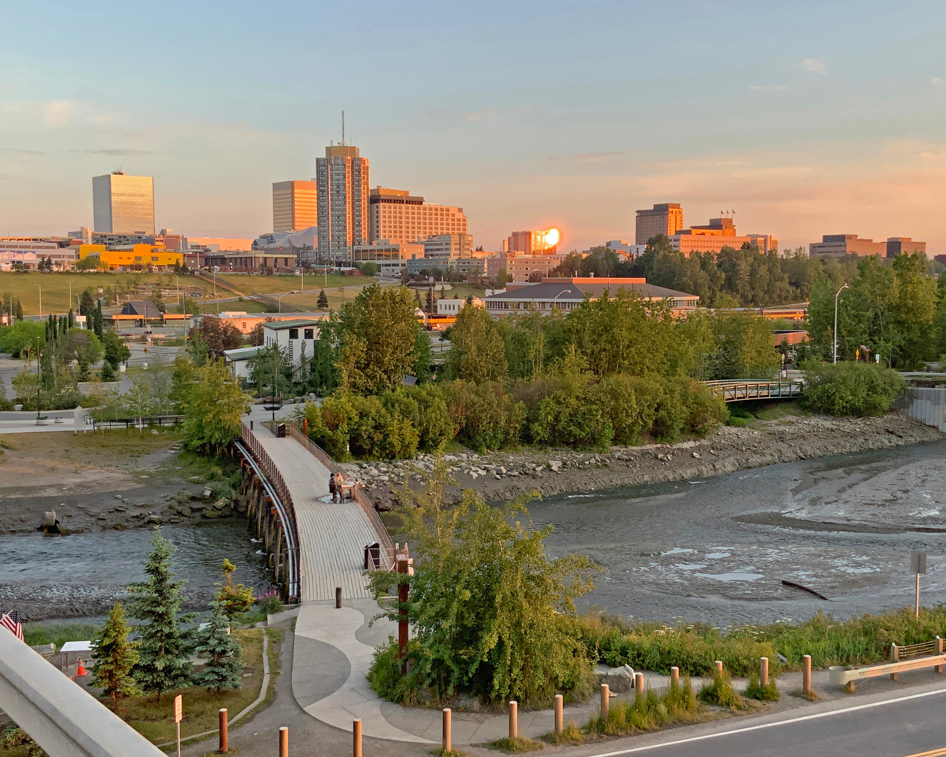 City skyline at sunset; pedestrian bridge over mudflats; buildings lit by golden light.