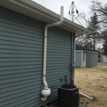 White exhaust pipe on a blue house siding, near an air conditioner, and gutter.