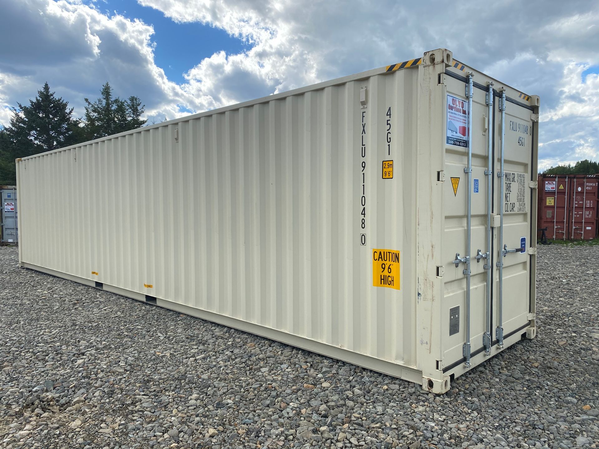 A beige, 40-foot shipping container sits on a gravel lot under a cloudy blue sky.