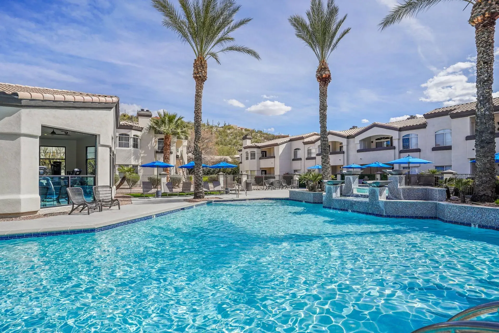 Resort-style swimming pool with palm trees and apartment buildings in the background at Pinnacle Heights in Tucson, AZ.