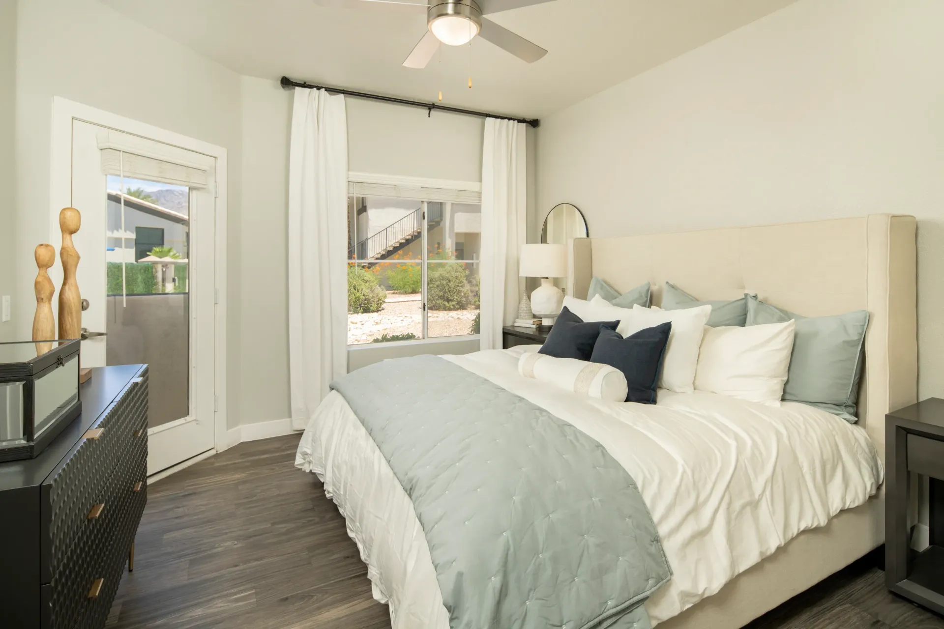 King-sized bed with plush pillows and a light blue comforter in a bedroom with a dresser and a window at Pinnacle Heights in Tucson, AZ.