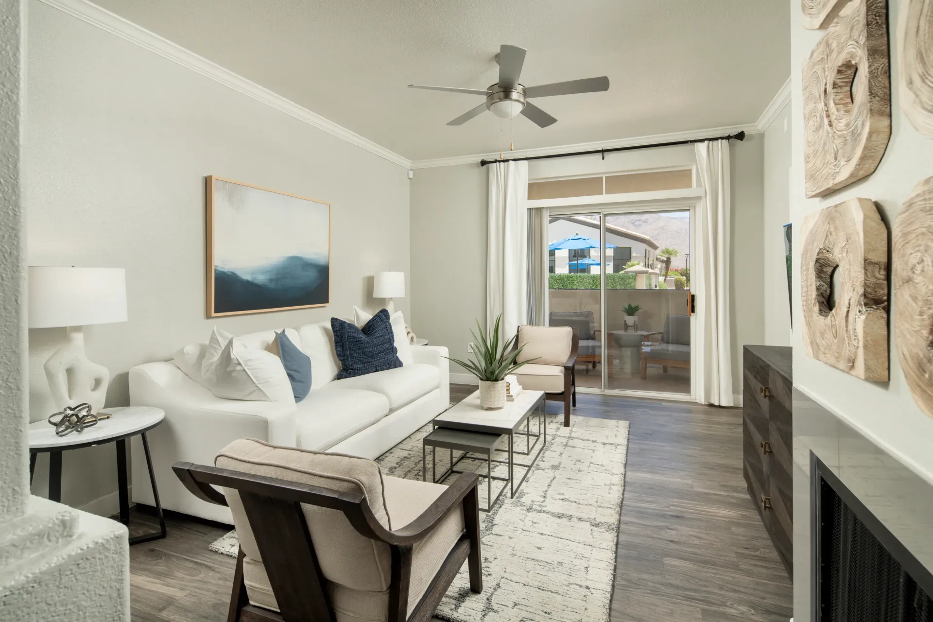 Modern living room with white sofa, accent chairs, coffee table, and sliding glass doors leading to a patio at Pinnacle Heights in Tucson, AZ.