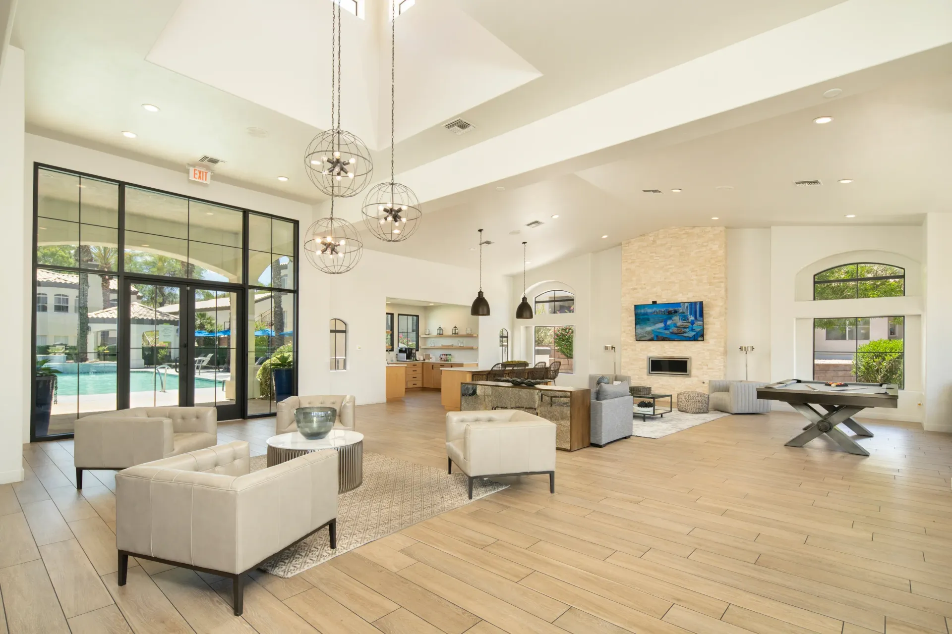 Modern clubhouse lounge with pool view, fireplace, pool table, and kitchen area at Pinnacle Heights in Tucson, AZ.