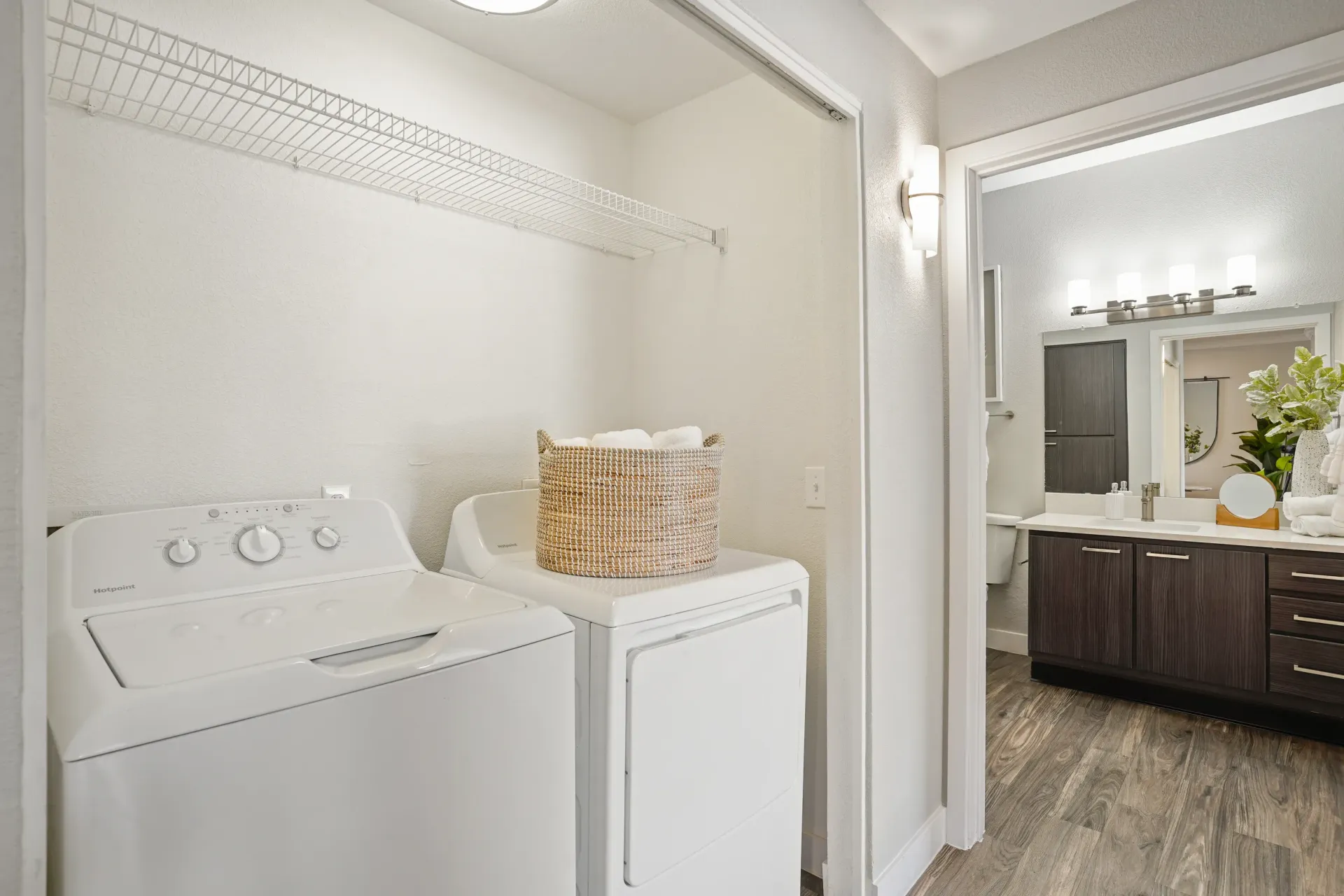 Washer and dryer in a laundry closet, with a basket of towels on top of the dryer. A bathroom vanity is visible through an open doorway at Pinnacle Heights in Tucson, AZ.