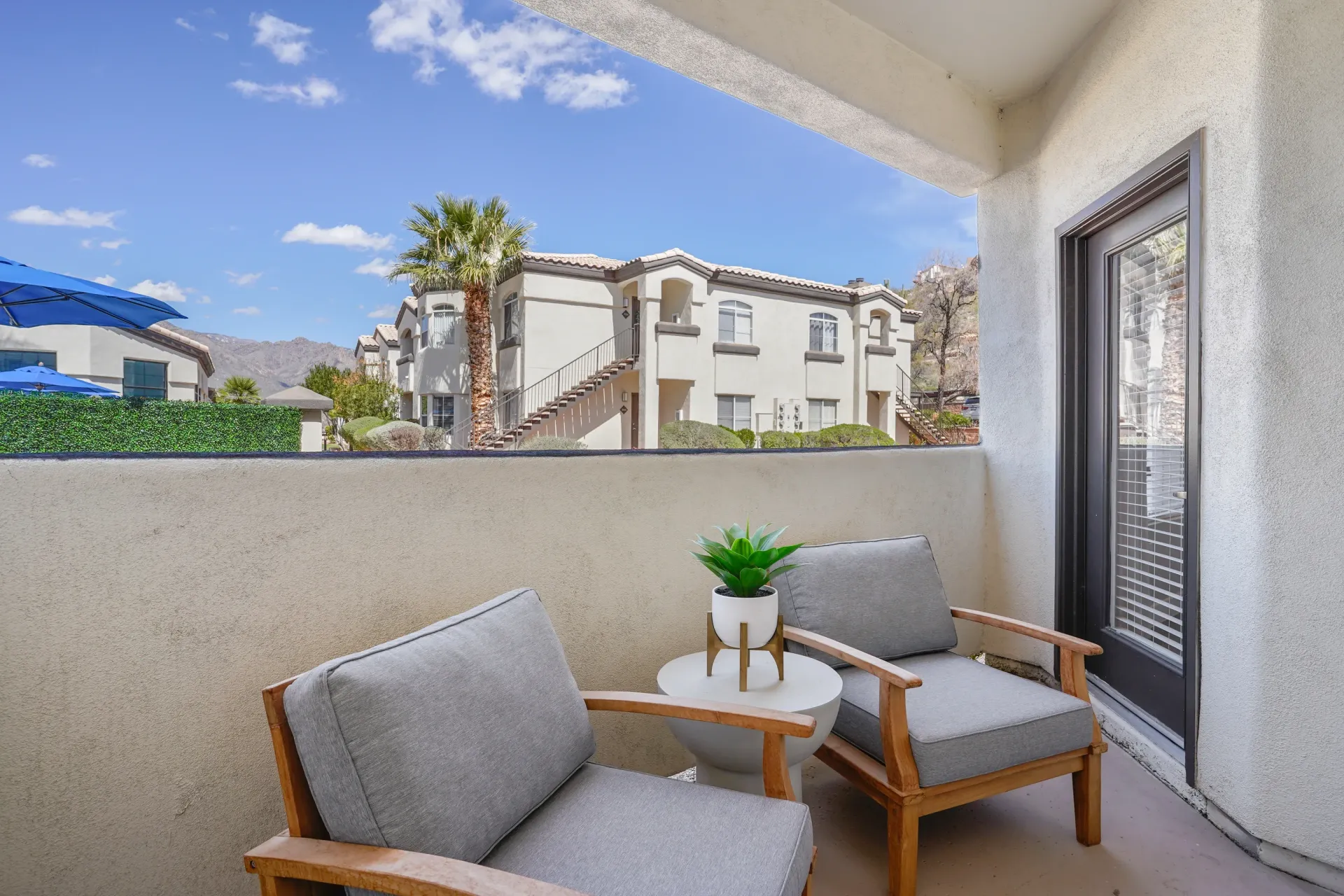 Balcony with two chairs and a table with a plant, overlooking apartment buildings at Pinnacle Heights in Tucson, AZ.