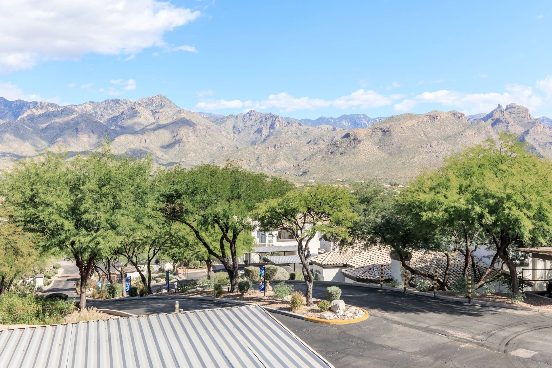 Exterior view of a desert apartment community with trees, parking, and mountain backdrop.