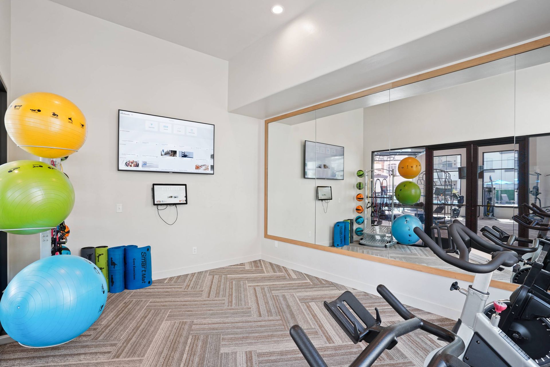 Gym area with cardio machines, a large wall mirror, and colorful exercise balls.