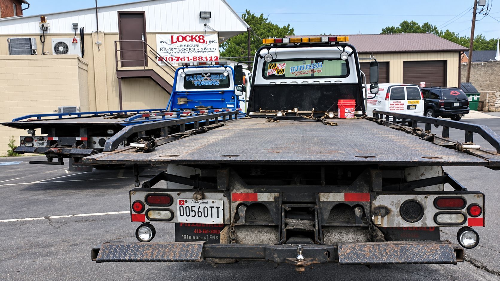 Tow truck lot with a flatbed trailer in the foreground and tow trucks parked behind it.