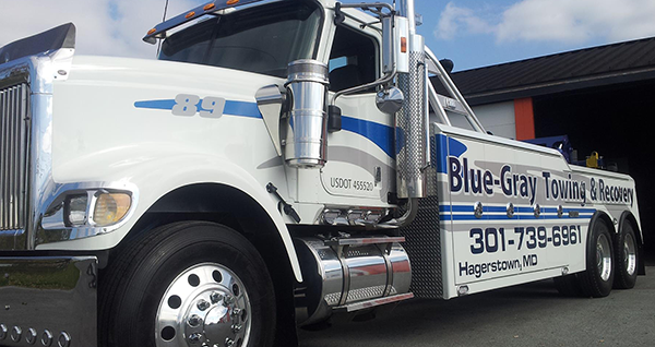 A blue gray towing truck is parked in front of a building.