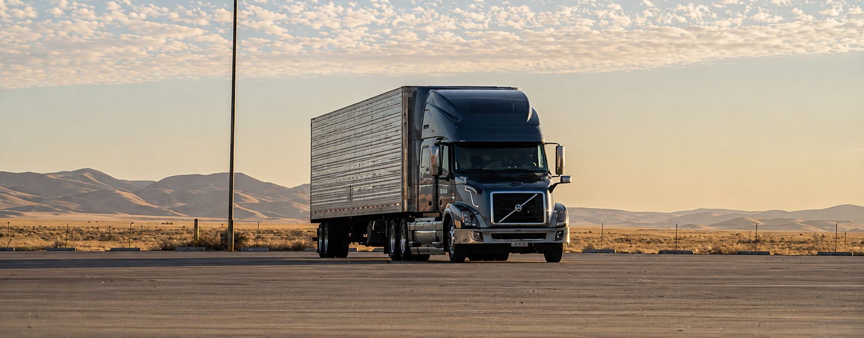 Blue semi-truck parked on a flat road at sunset with desert mountains in the background