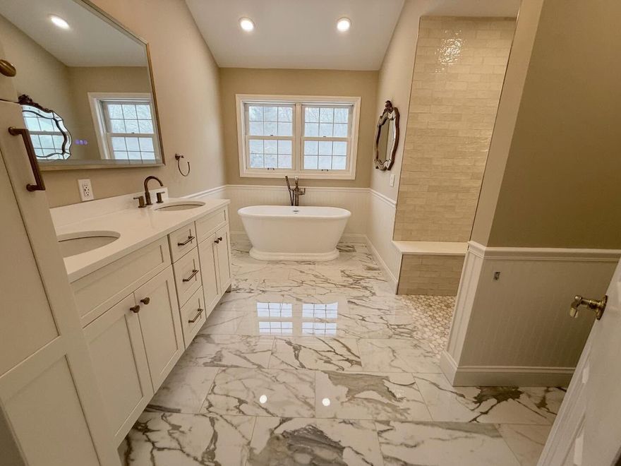 Bright modern bathroom with marble floor, freestanding tub, double vanity, and glass shower niche.