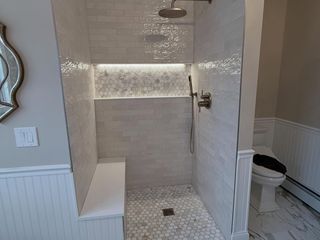 Walk-in tiled shower with bench, rainfall showerhead, and built-in shelf in a bathroom