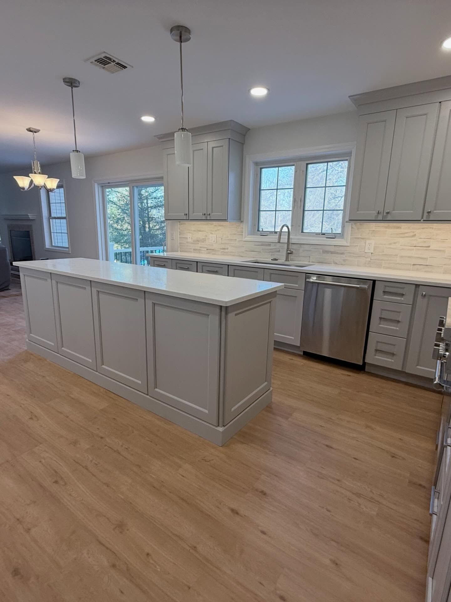 Bright kitchen with gray cabinets, white island, stainless dishwasher, and hardwood floors
