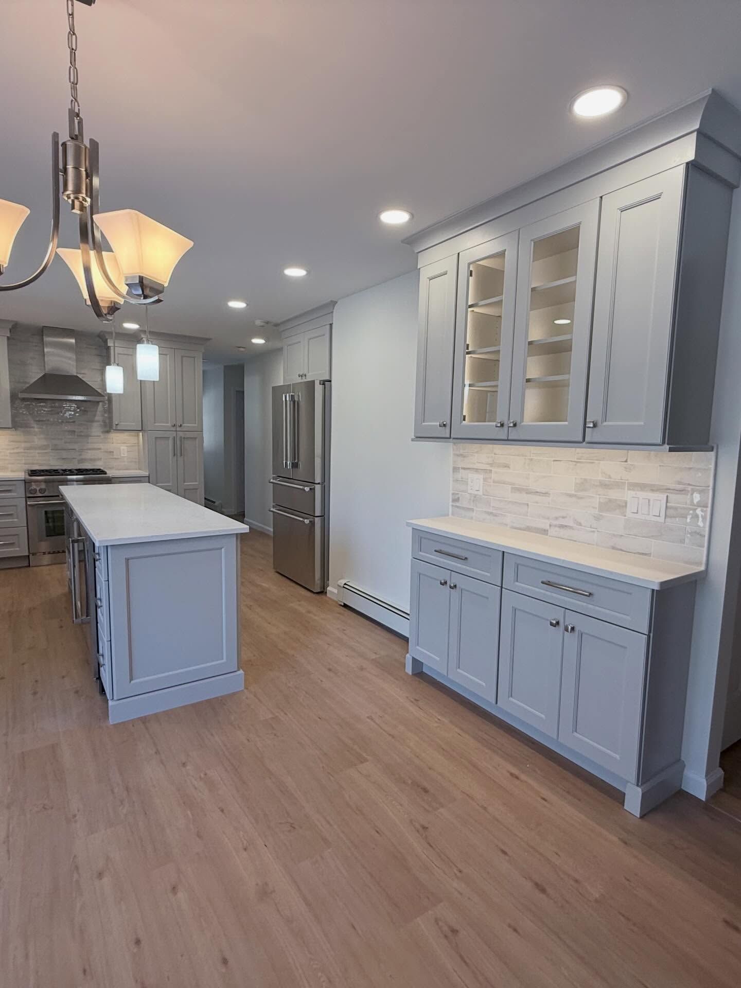 Bright modern kitchen with gray cabinets, white countertops, island, and stainless steel appliances.