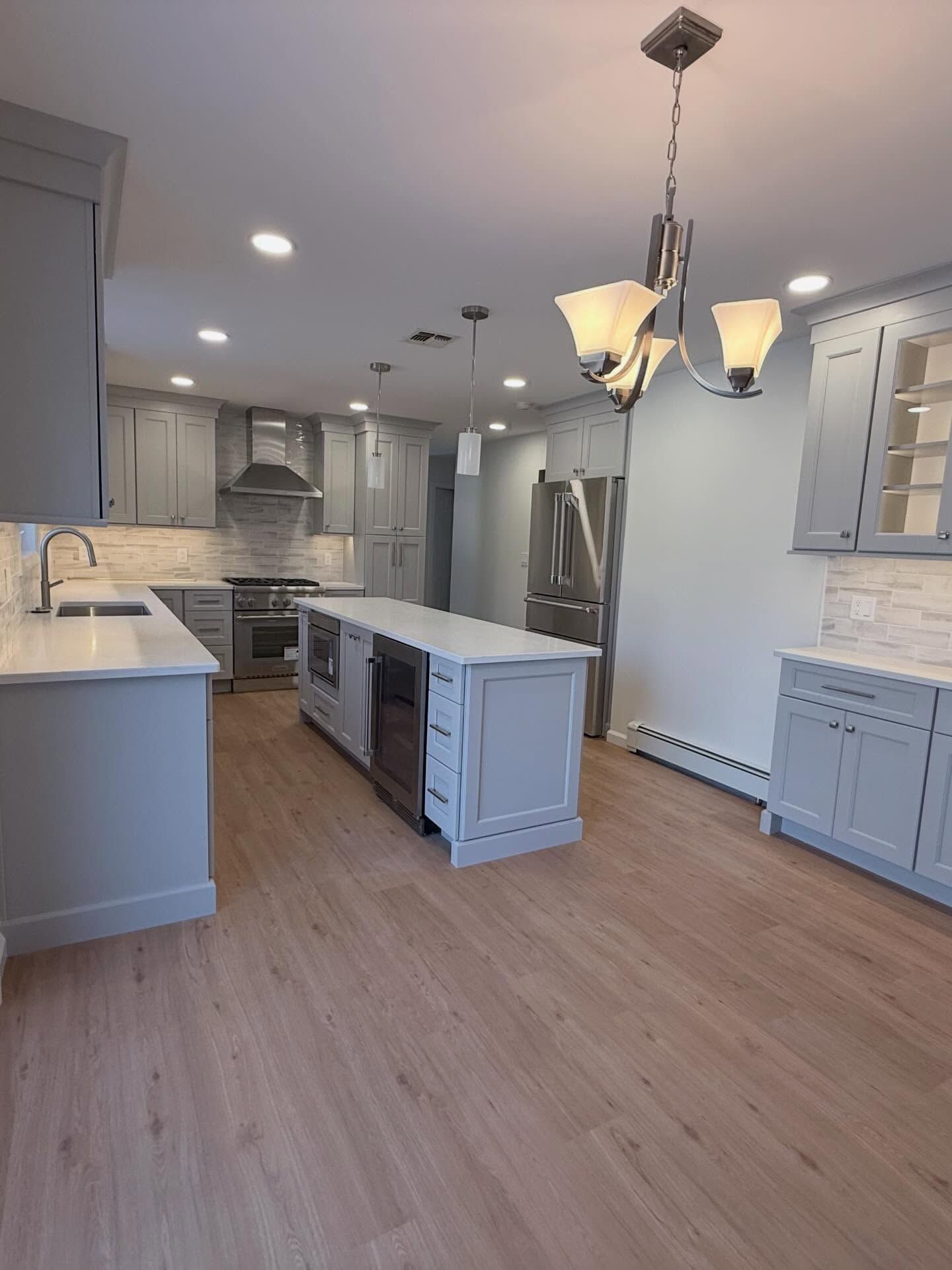 Bright modern kitchen with white cabinets, gray island, stainless appliances, and wood flooring