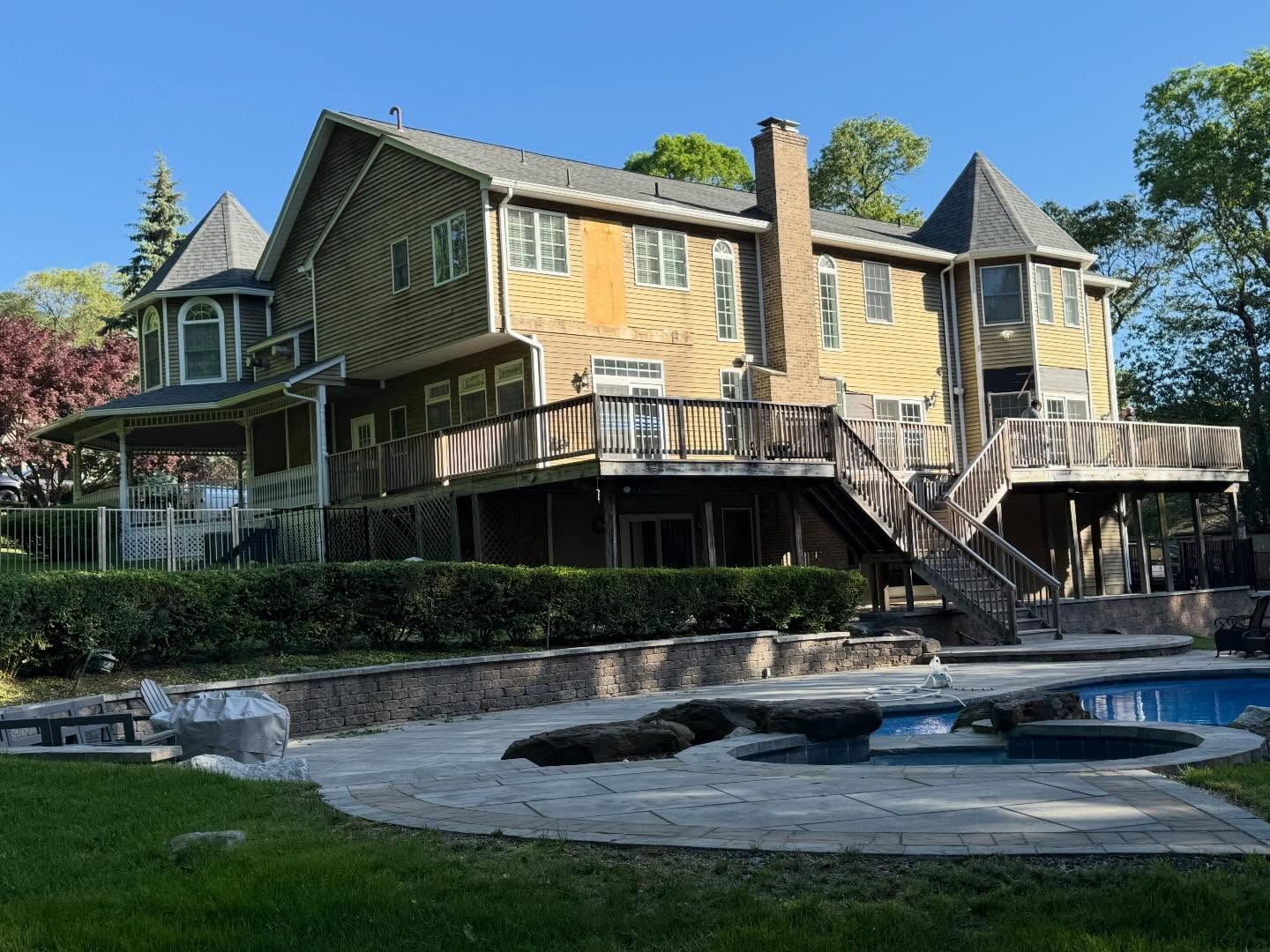 Large yellow house with wraparound deck and a blue pool under a clear sky