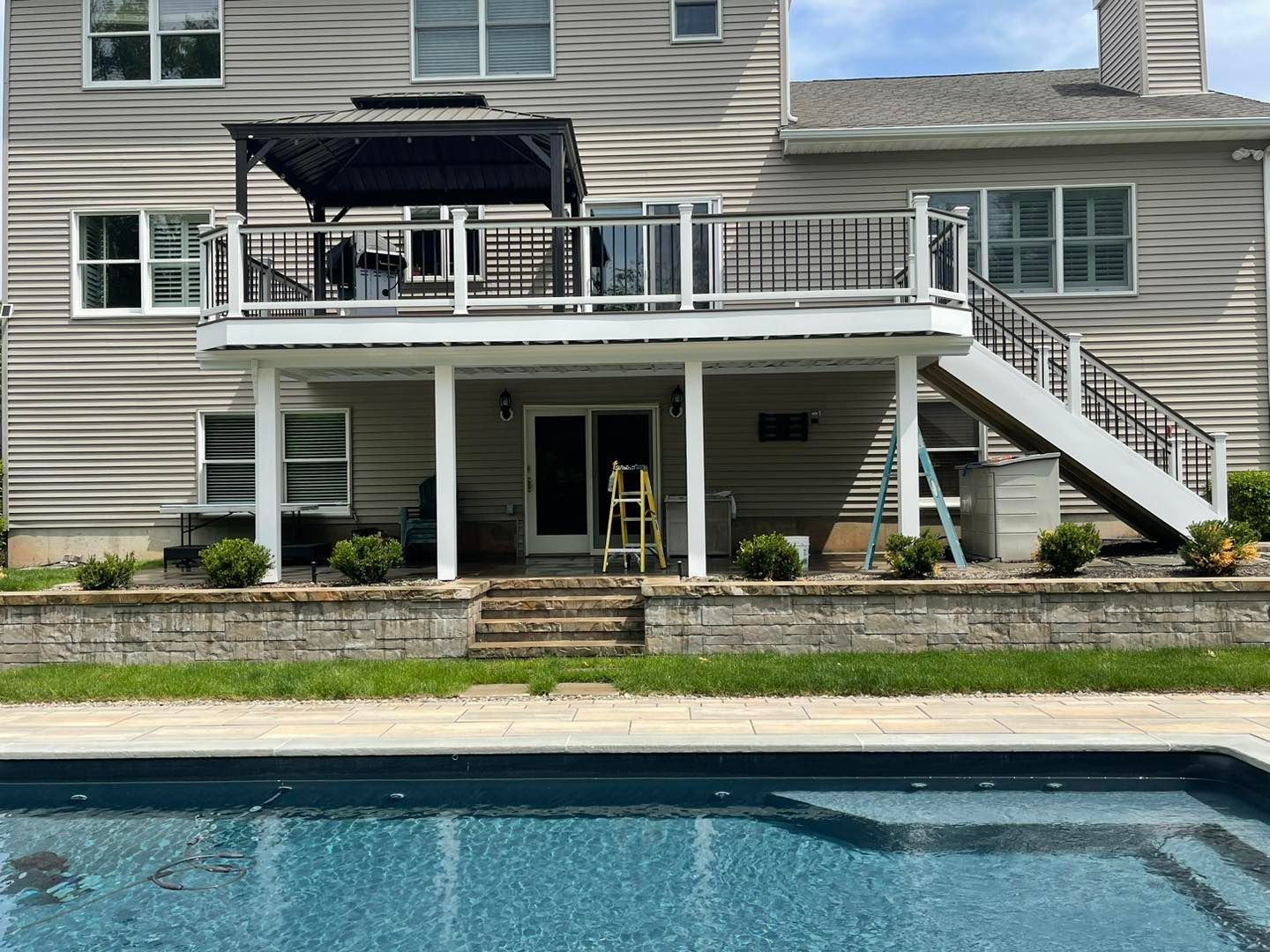 Backyard deck with patio furniture and stairs beside a house, overlooking a swimming pool
