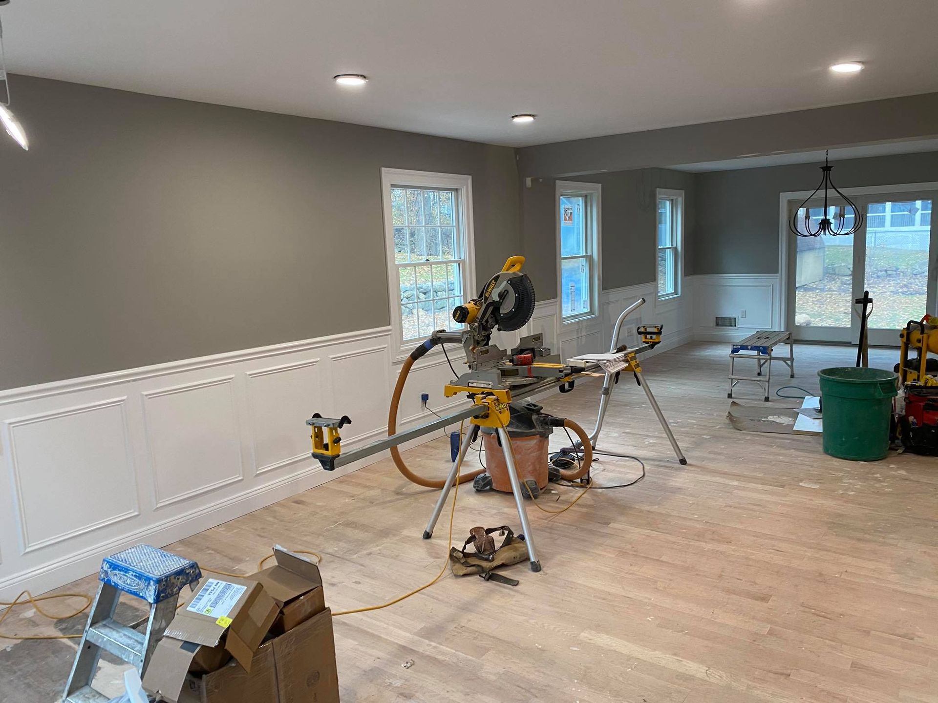 Room under renovation with gray walls, white wainscoting, and a miter saw on a stand amid tools and debris