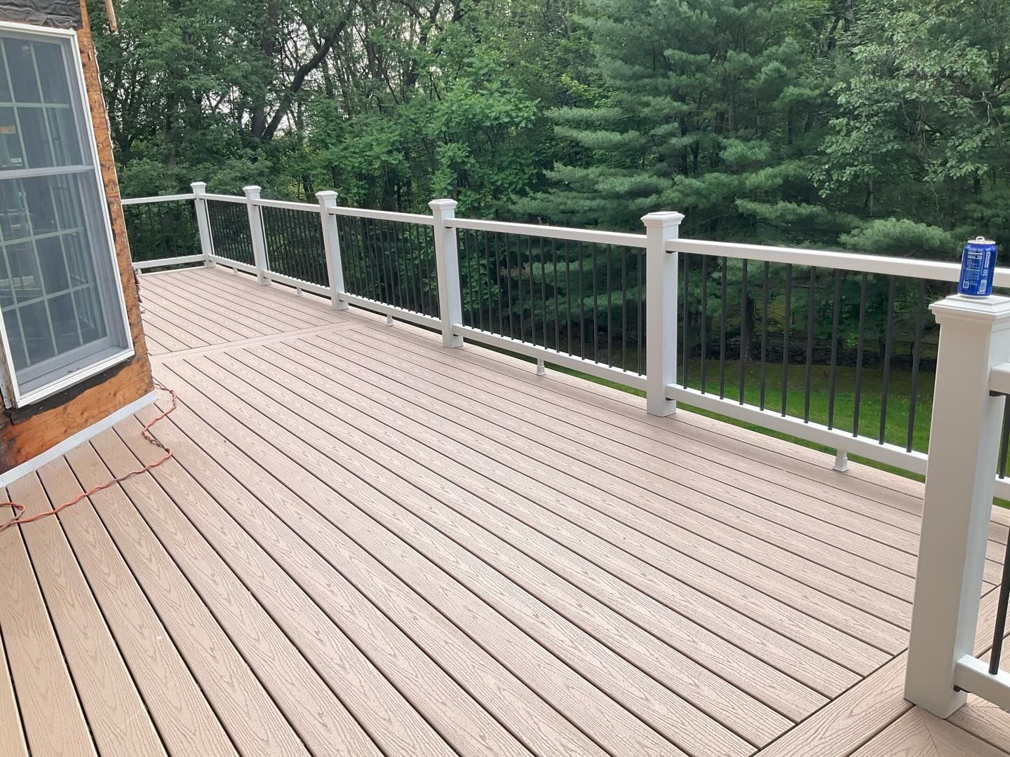 Wooden deck with white railing overlooking a green yard and trees, beside a house window