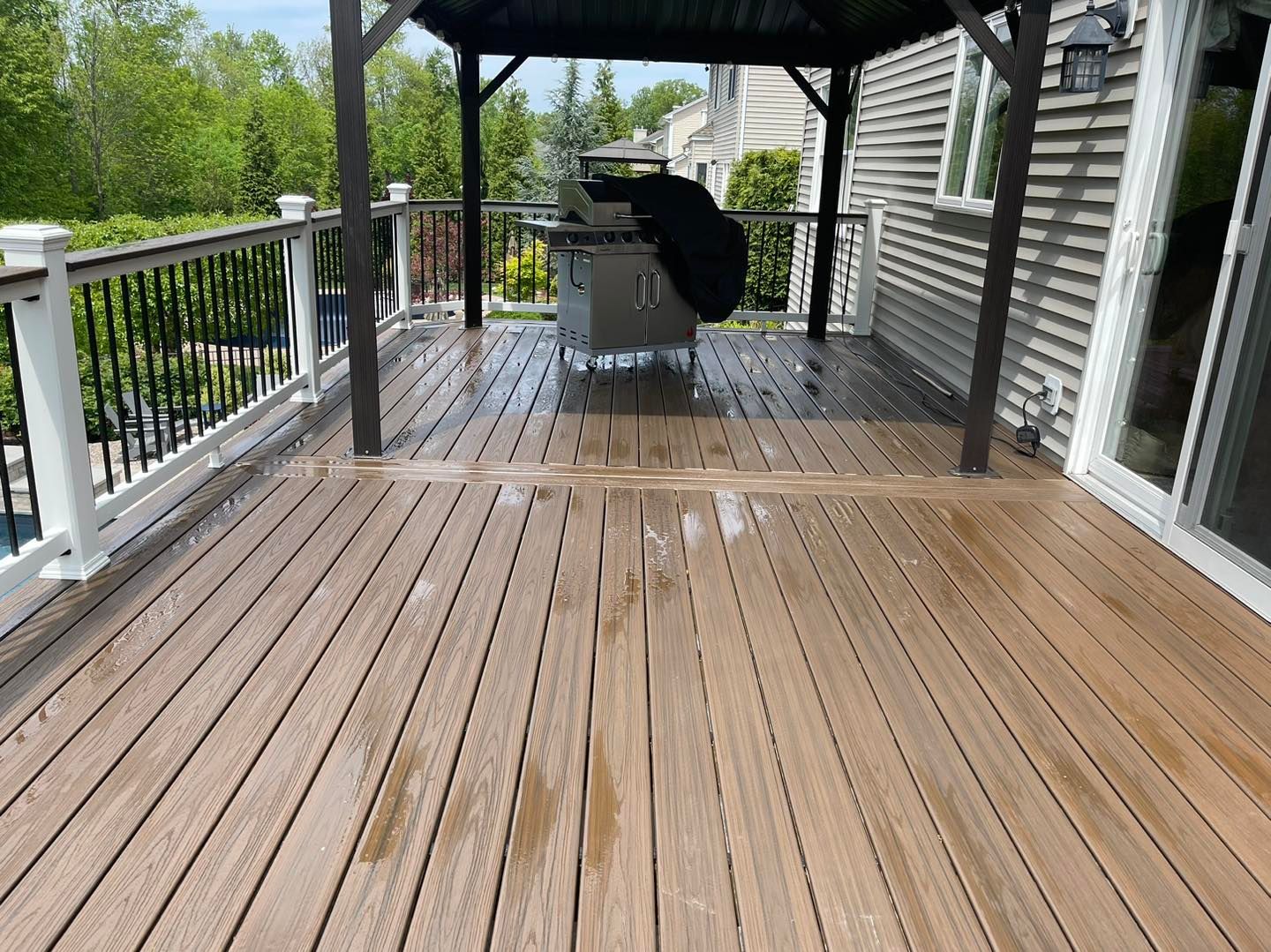 Wooden deck with gazebo and railing, a black dog resting by outdoor furniture on the covered patio.
