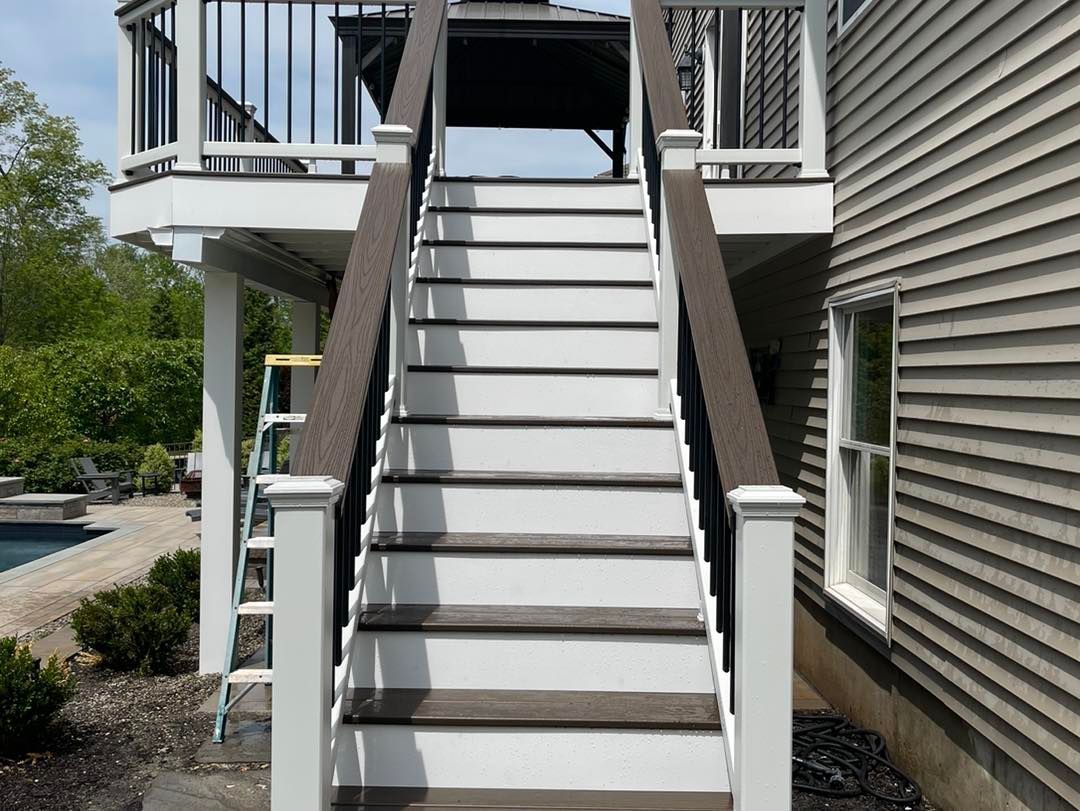 Outdoor staircase with white steps and railings beside a house, leading up to a deck.