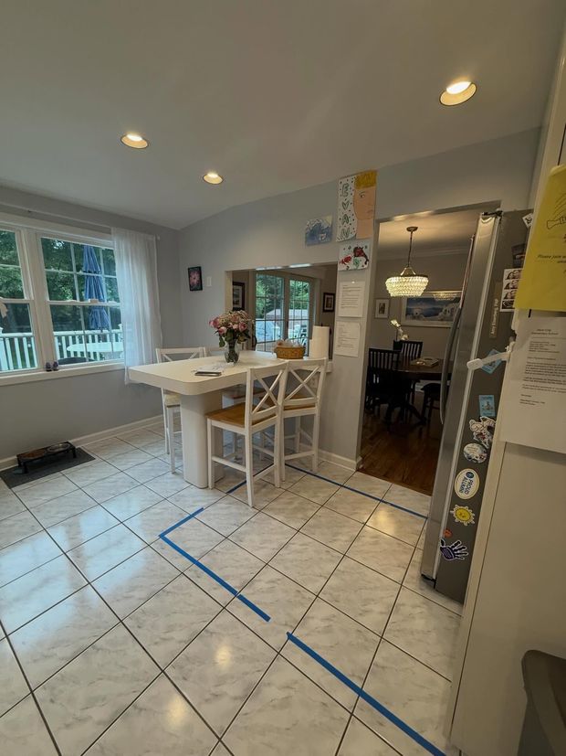 Bright kitchen with white tile floor, island table, pendant lights, and doorway to a darker room