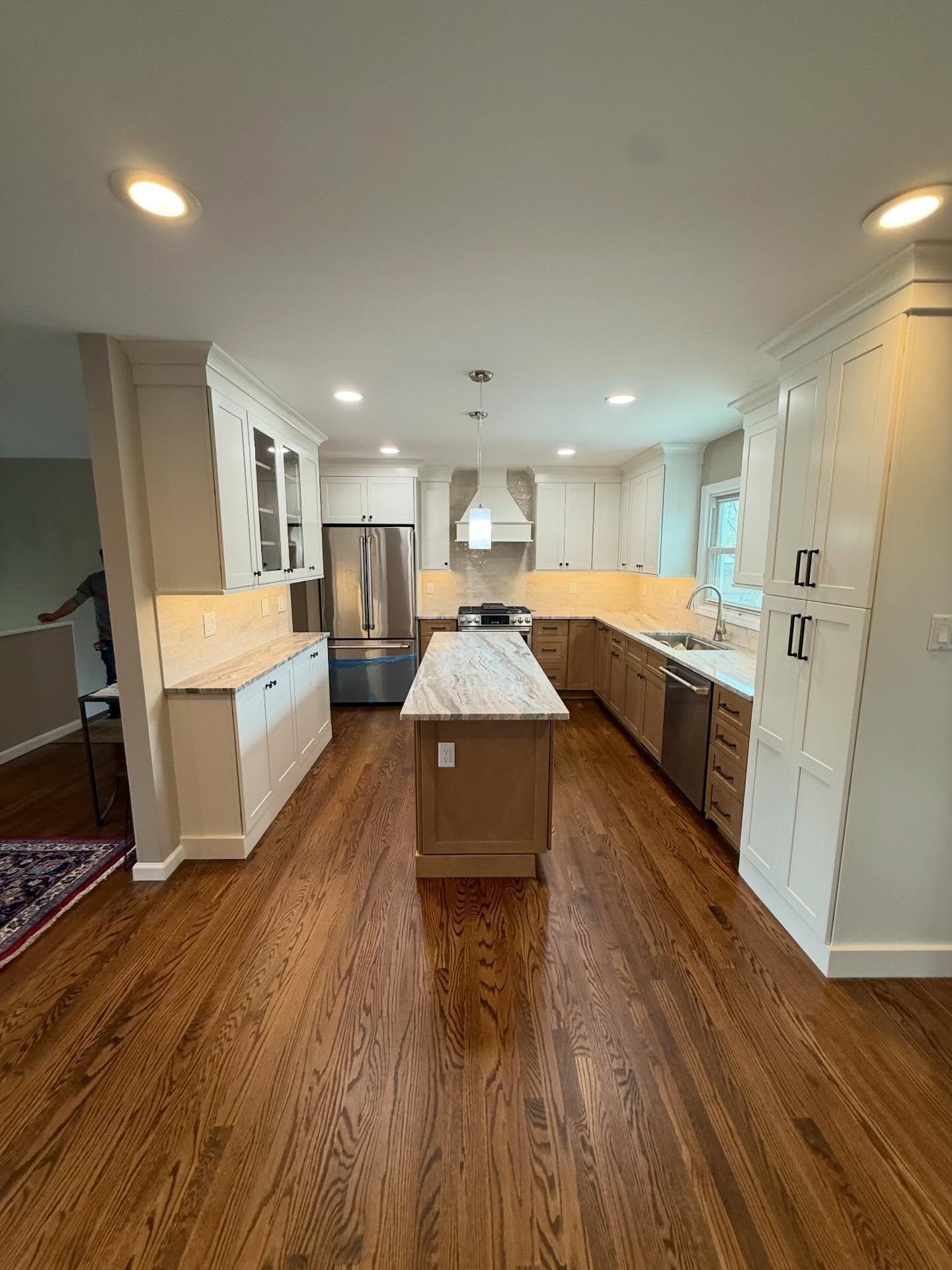 Modern kitchen with stainless appliances, white cabinets, wood floors, and a central island.