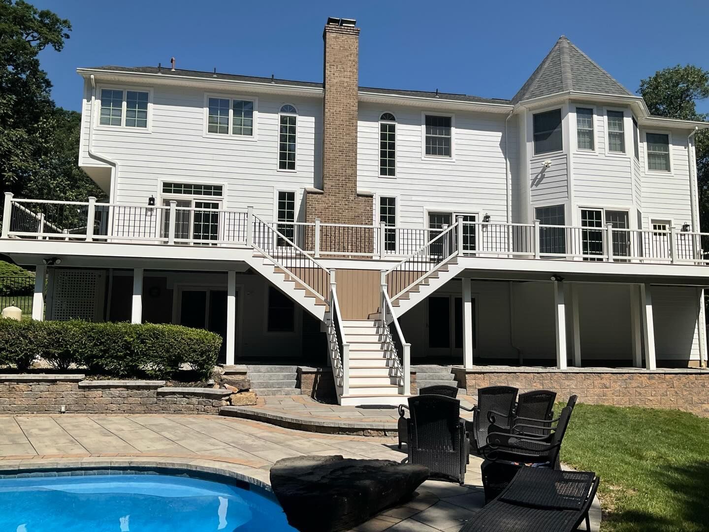 White two-story house with a large deck, central staircase, and a blue swimming pool in the yard