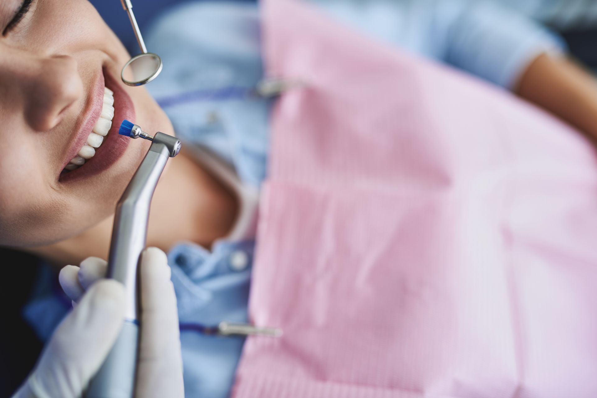 Un dentista utilizza uno strumento per lucidare i denti di un paziente, tenendo in mano uno specchietto dentale.