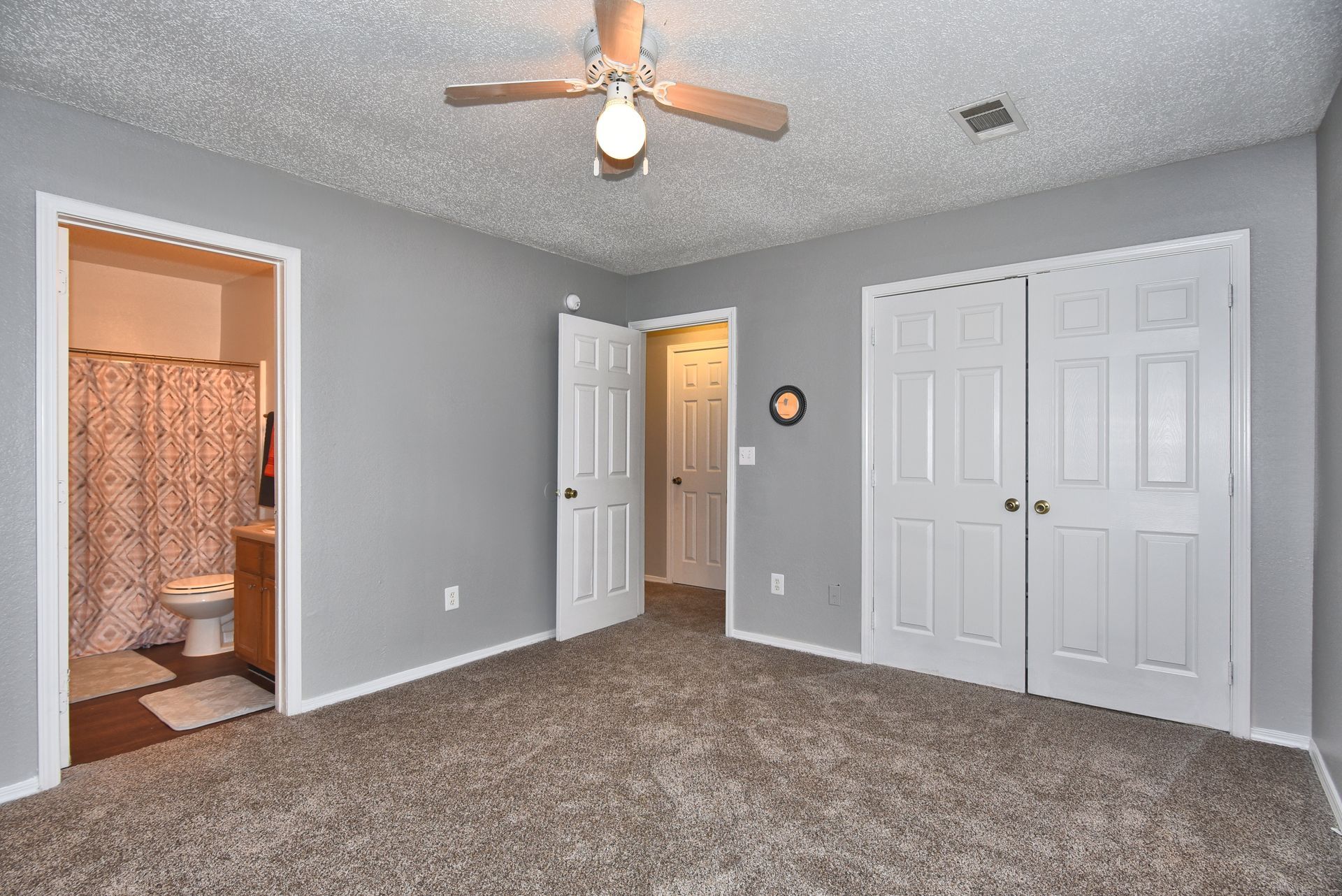 Empty gray bedroom with carpet, ceiling fan, open doorway, and white closet doors