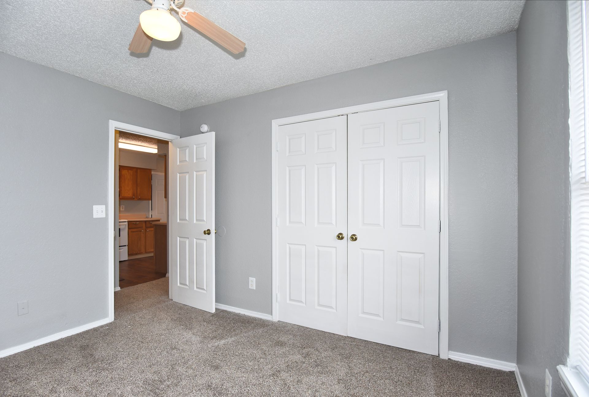Empty gray bedroom with carpet, ceiling fan, open door, and white closet doors