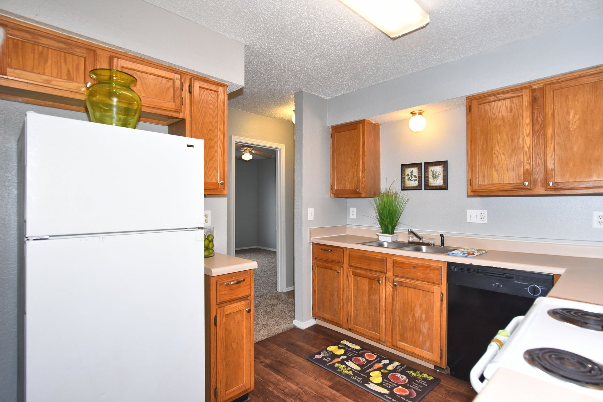 Kitchen with white appliances, wooden cabinets, and a sink under a bright ceiling light.