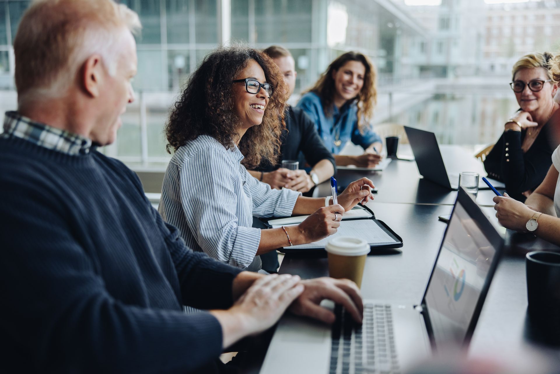 People in a meeting around a conference table with laptops and notebooks in a bright office