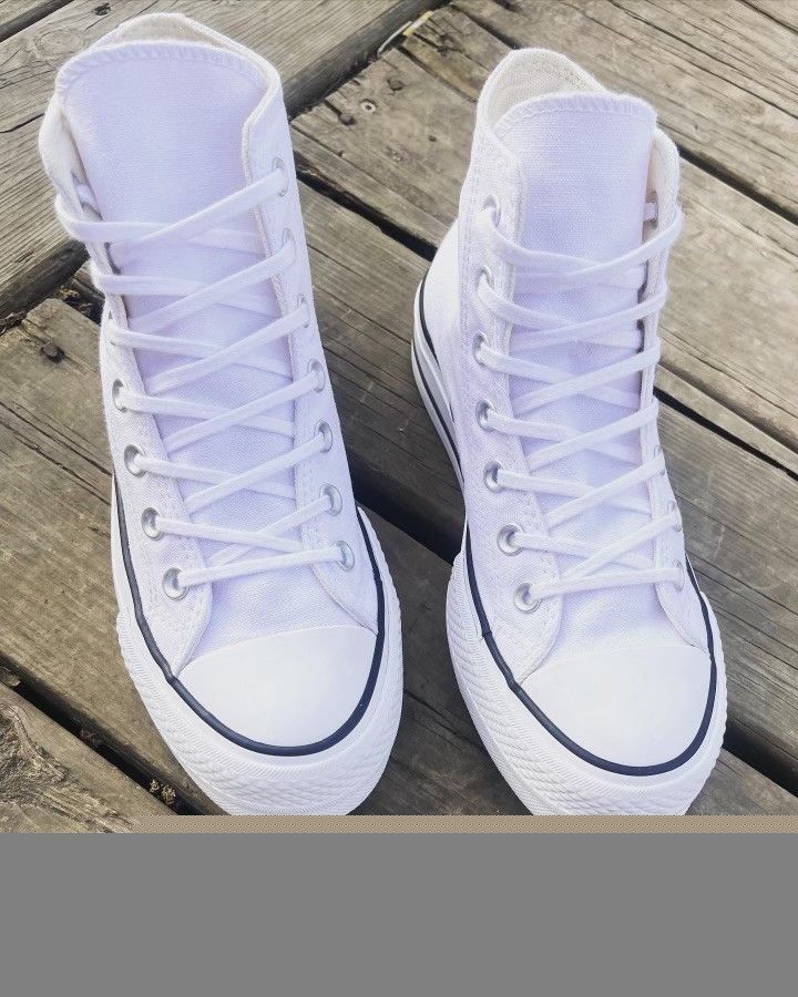 A pair of white converse shoes are sitting on a wooden surface.