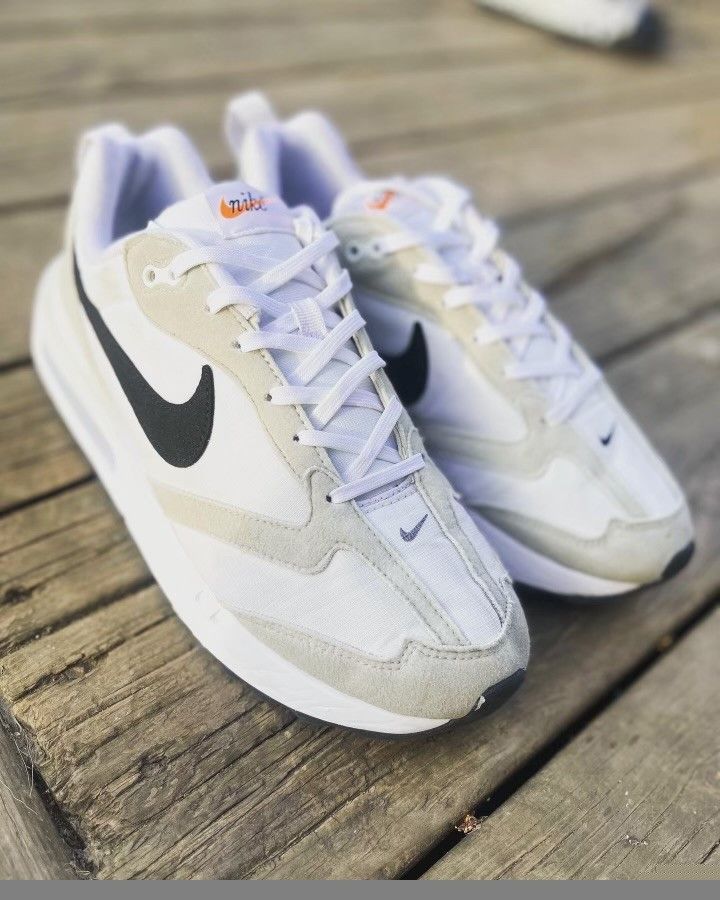 A pair of white nike sneakers are sitting on a wooden surface.