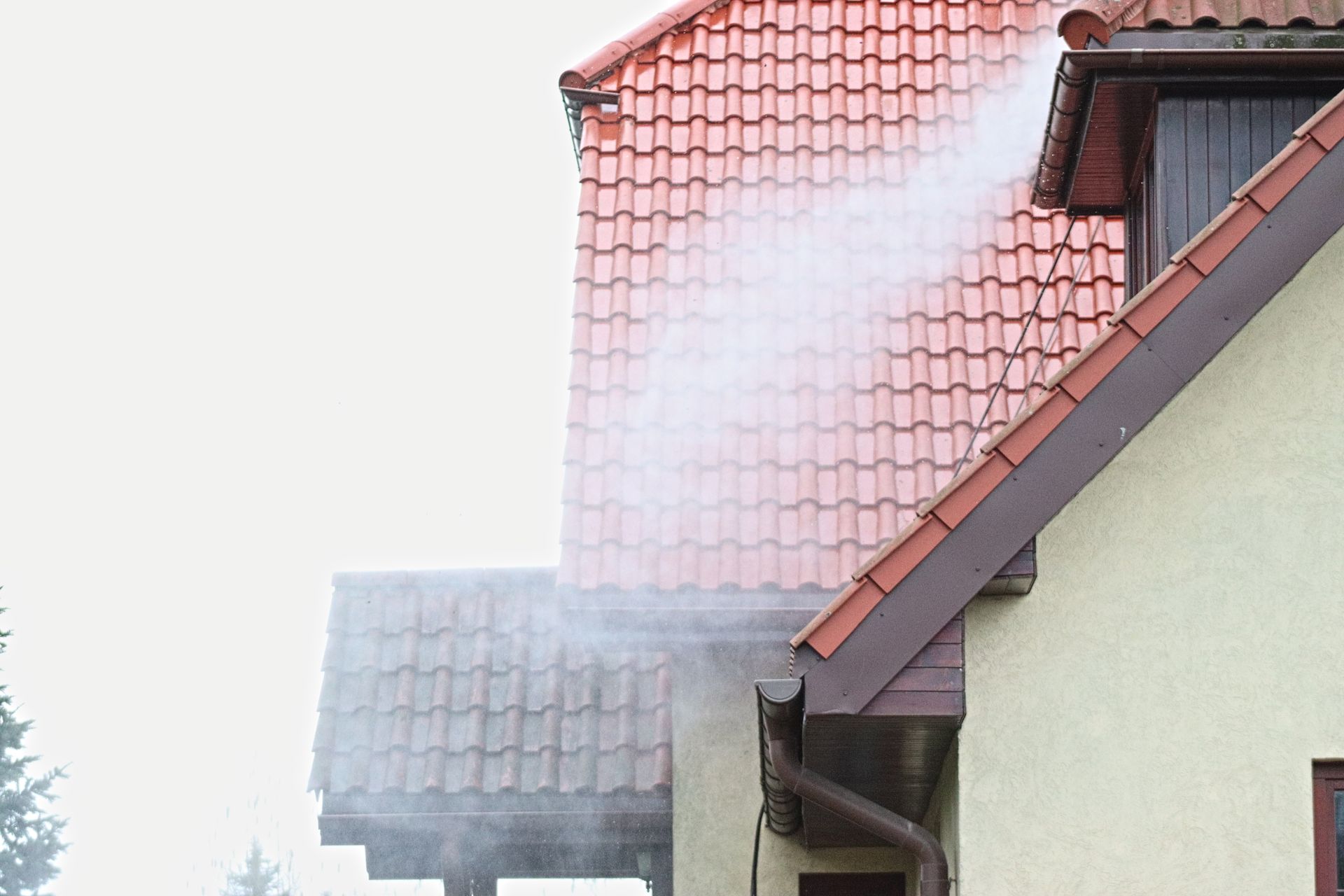 Roof chimney venting white steam beside a house with red tile roof and beige siding