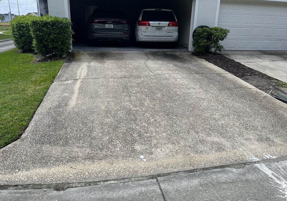 Concrete driveway leading to a garage with two parked cars and trimmed bushes on either side.