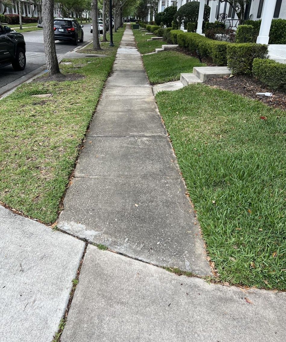 Sidewalk with grass lawns, trees, and parked cars along a residential street
