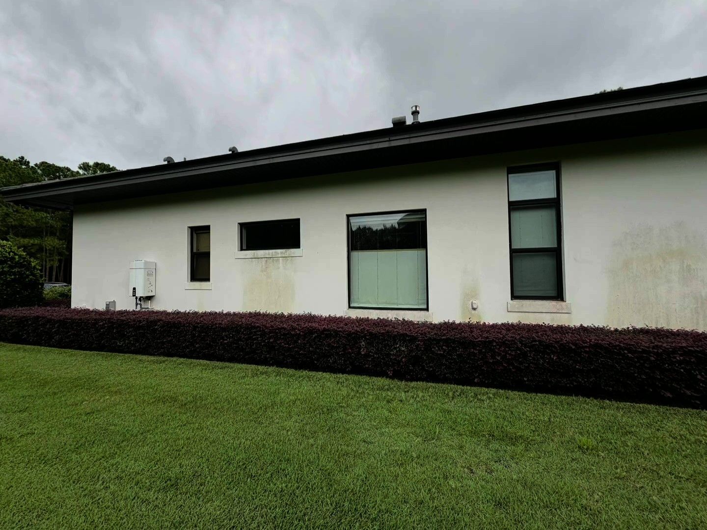 Single-story white house with black roof, dark windows, and trimmed hedge along a green lawn