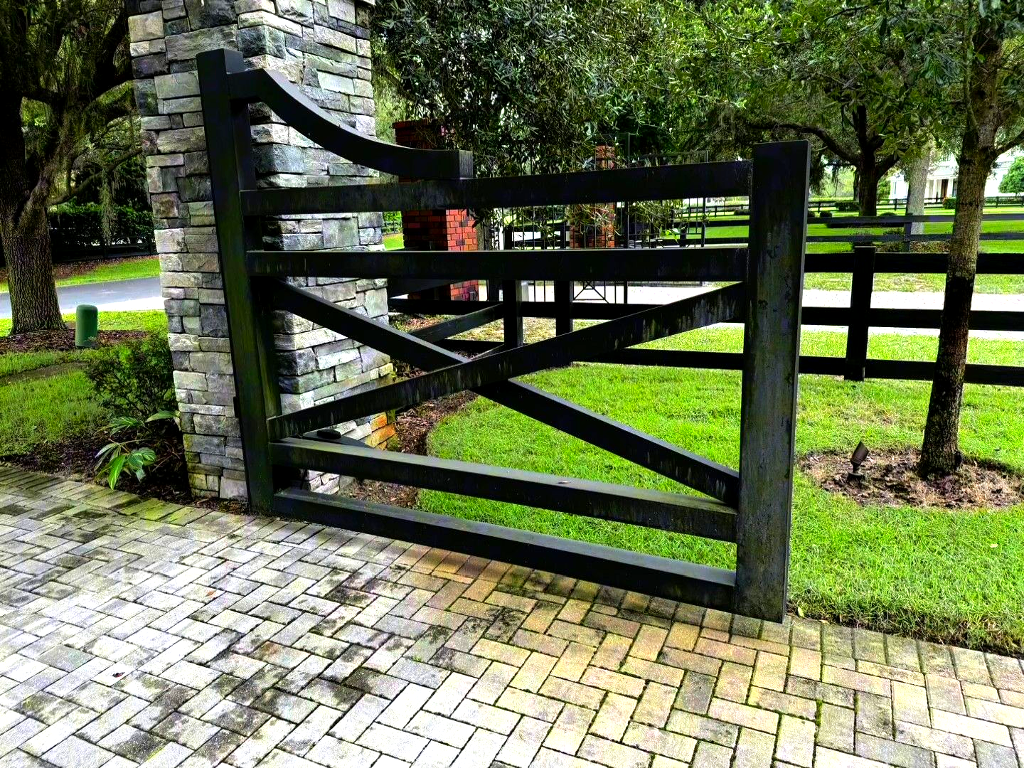 Black wooden gate in a cobblestone path beside a green lawn and trees