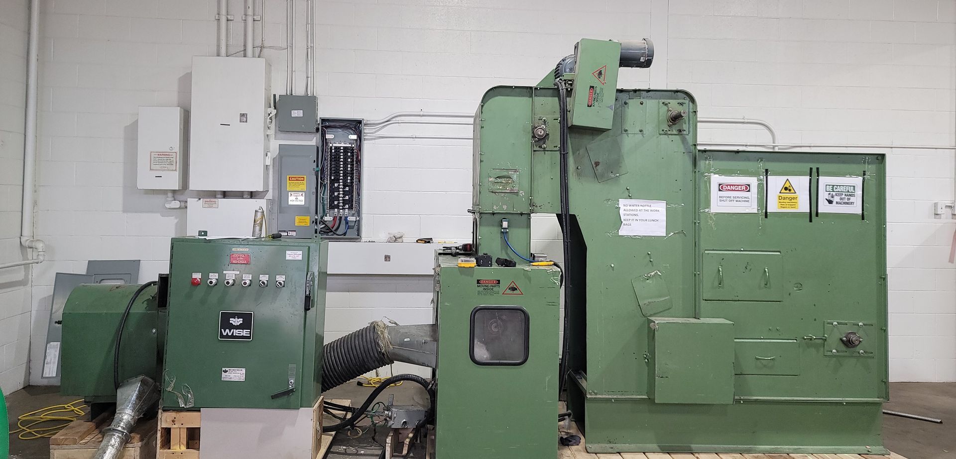 A large green industrial machine with various control panels and electrical boxes in a factory setting.
