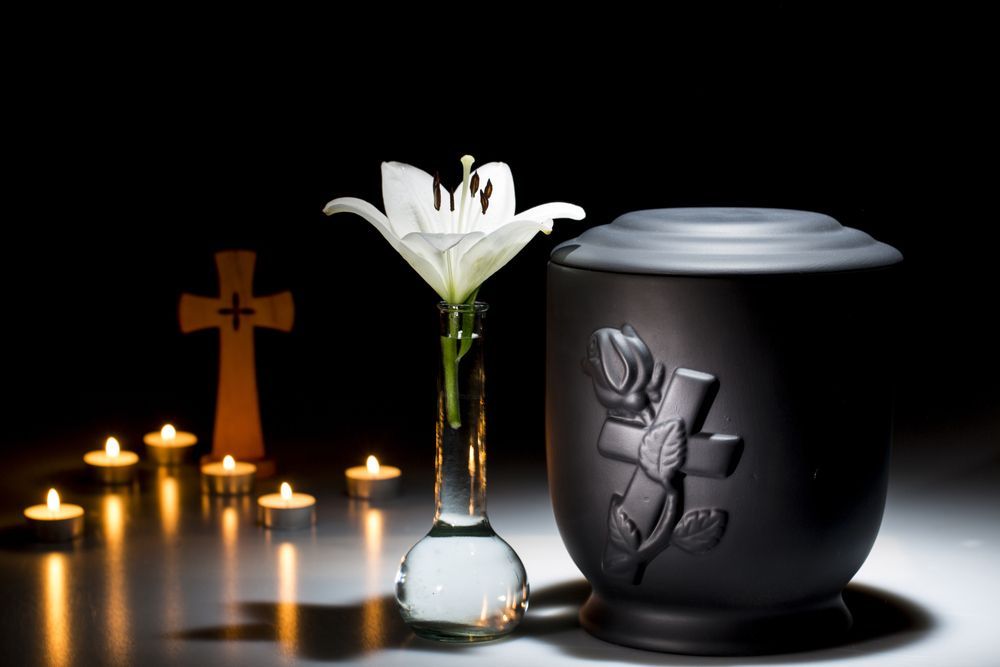 A Black Urn With A Cross On It Is Next To A Vase Of Flowers And Candles — Northern Rivers Headstones in Kyogle, NSW