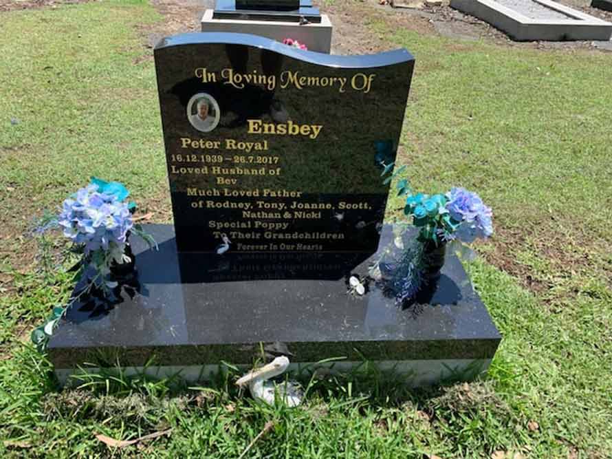 A Black Gravestone With Blue Flowers On It In A Cemetery — Northern Rivers Headstones in Casino NSW